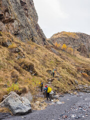 Obraz premium Autumn trekking on footpath alone Caucasus rocks. Group of tourists with backpacks climbs the mountains along the autumn trail.