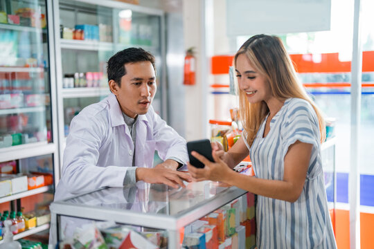 male pharmacist behind display case serving female customer in pharmacy