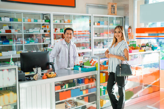 Attractive asian woman smiling at camera while male pharmacist working at pharmacy