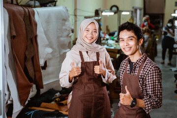 hijabi craftswoman and craftsman smiling with thumbs up in leather tannery workshop