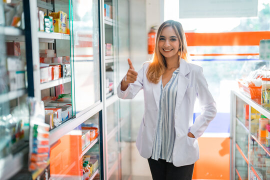 beautiful pharmacist woman in uniform smiling with thumbs up camera at pharmacy