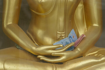 A golden statue of Buddha holds Thai money 50 Baht in its palms