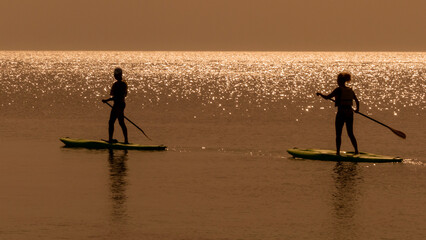 tourists relax on SUPs in the flat sea at sunset