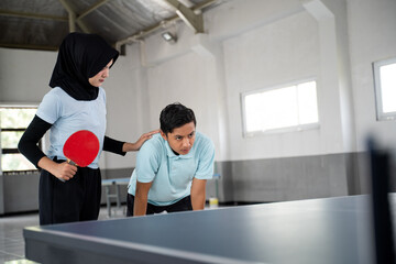 female athlete in hijab helps male partner go weak during a ping pong match