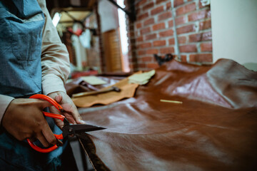 Obraz premium Hands of craftswoman cutting while working at table in leather fabric in studio