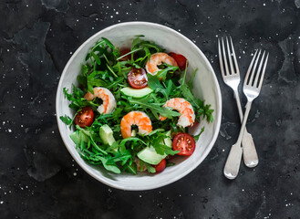 Salad with shrimp, arugula,avocado, cherry tomatoes on a dark background, top view