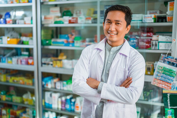 male pharmacist in uniform smiling with crossed hands on pharmacy display case background