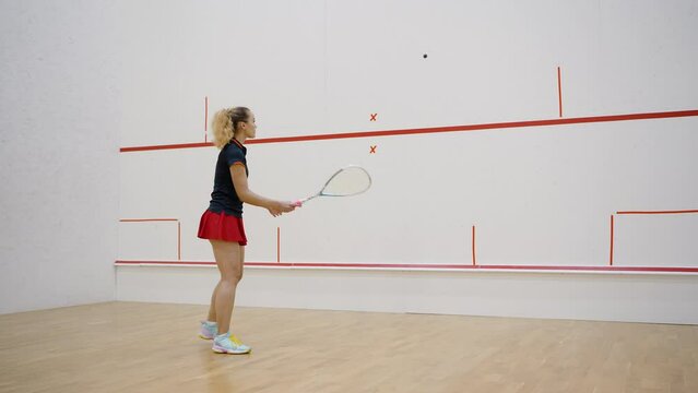 Young lady in sportswear trains in squash court alone