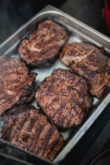 Ready steaks after grilling cooling down before being cut in restaurant metal tray