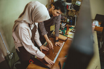 craftsman and craftswoman wearing hijab using a ruler measuring leather patterns in a leather workspace