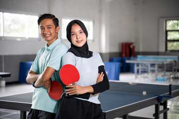 Mixed doubles ping pong athletes holding bats standing back to back with crossed hands on ping pong...