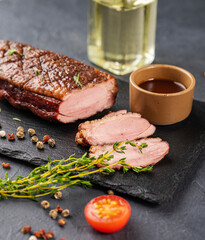 Grilled BBQ duck breast in marinade and spices with sauce on a slate board with fresh herbs on a dark background close up.