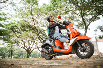 Fototapeta na wymiar Cheerful student girl wearing helmet and jacket riding motorbike to school