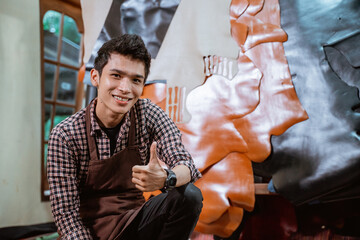 Smiling craftsman with thumbs up against leather materials background in workshop