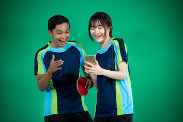 Asian female and male athletes excited to look at smartphones while playing ping pong