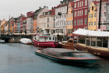 Long exposure of tour boat passing in front of Nyhavn a canal and entertainment district lined by brightly coloured 17th & 18th-century townhouses, in Copenhagen during the day