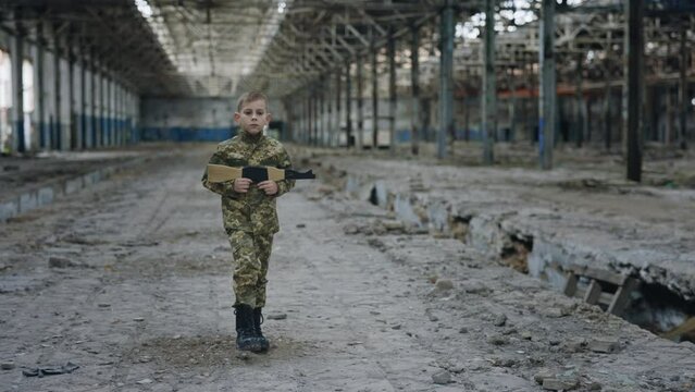 Little soldier is marching holding a toy gun against a background of devastation place. Military wear. War. Patriot