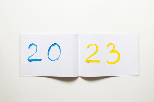 2023 painted with yellow-blue paints as the color of the flag of Ukraine on a white scrapbook on a white background, Happy New Year 2023