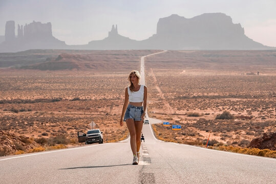 Tourist walking on road amidst landscape at Monument valley. Woman is exploring desert with car parked in background at Navajo Tribal Park. She is enjoying summer vacation.
