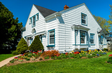 An older style tradional home with flower beds full of springtime flowers. - 557475309