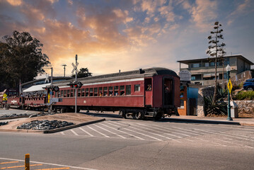 Santa Cruz, USA. September 20, 2022. Vintage red train moving on street with cloudy sky in the background at Santa Cruz Beach Boardwalk during sunny day