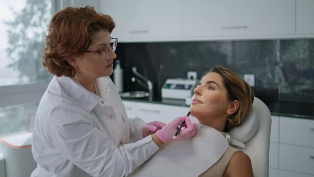 Beautician drawing correction lines on woman face before lifting procedure.