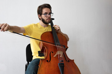 young cello player practincing in a white room, young man playing violoncello at home practicing music teaching from home