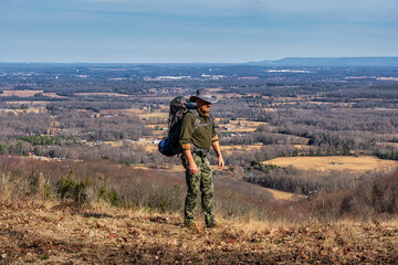 A man walking on a hiking trail with a backpack, camping on a mountain bluff overlooking the valley with Winchester Tennessee in the background.