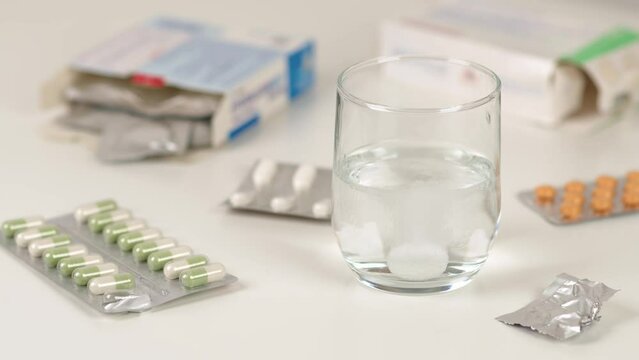 Comprim&eacute; d'aspirine effervescent dans un verre d'eau avec des m&eacute;dicaments autour