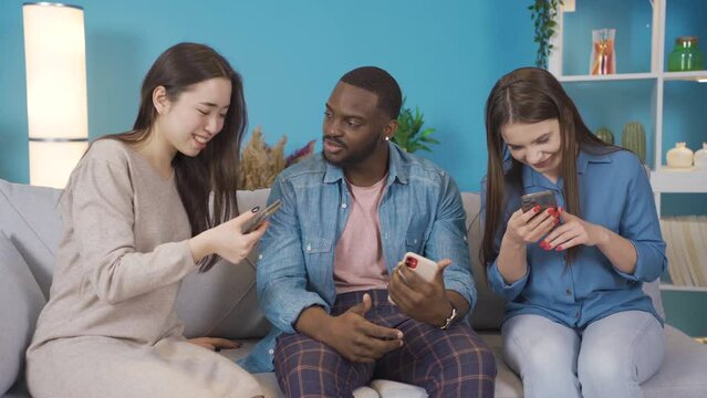 Young people of different races are using phone at home and showing phone to each other.
Asian, European and African youth use phones at home. They are showing each other something on the phone.
