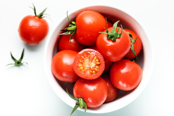 Fresh tomatoes in bowl on white table. Top view, copy space. Red cherry tomato stack on white background. fresh tomatoes with water drops on white background.
