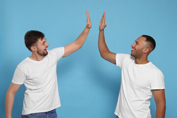 Men giving high five on light blue background