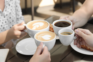 Friends drinking coffee at wooden table in outdoor cafe, closeup