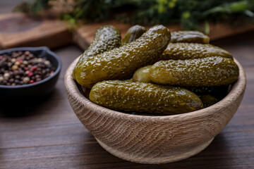 Bowl of pickled cucumbers and ingredients for food preservation on wooden table, closeup