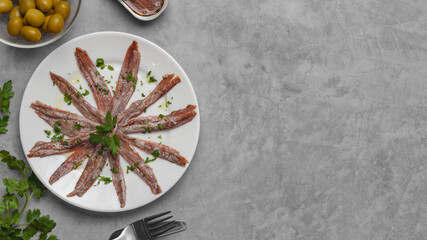 Delicious anchovy fillets, served with olives and parsley on grey table, flat lay. Space for text