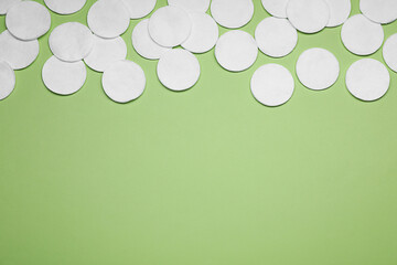 Many cotton pads on green background, flat lay. Space for text