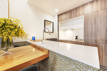 Open plan kitchen island with white marble countertop with integrated sink and another wooden countertop with a flower arrangement