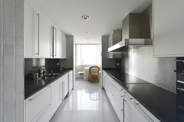 elongated kitchen with black marble countertop on white furniture with large drawers on both sides of the room