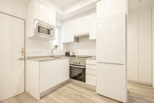 Small open plan corner kitchen with white handleless cabinets and a white built-in fridge