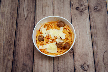 A bowl of spaghetti bolognese with tomato, beef meatballs, lacquers of Parmesan cheese in a delivery bowl