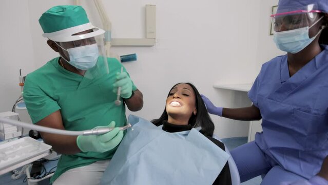 Dental visit in a clinic, African dentist checks the dental health of his patient together with the assistant.