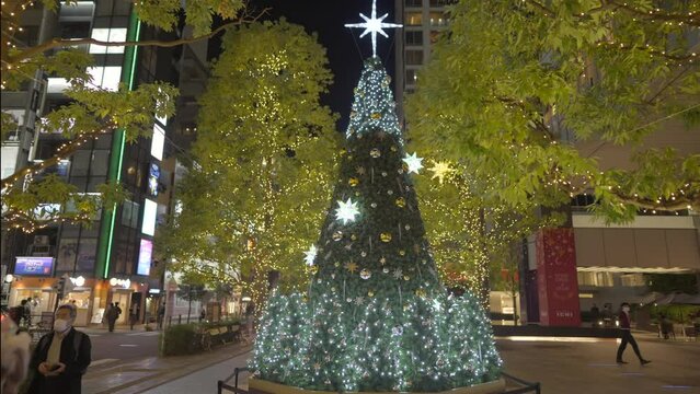 This video shows a lit up Christmas tree on display in the city at night.