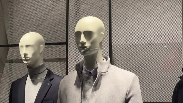Male mannequins in a classic jacket and coat stand in the clothing store window