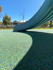 Shadow on perforated playground. Padded floor covering with rubber granules. Kids slide. Playground equipment. 