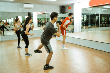 Obraz premium instructor performs thigh muscle exercises with the sporty group in front of the mirror at the fitness center