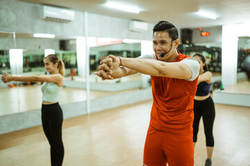 male instructor leading exercise with hand muscle stretching movements in fitness center