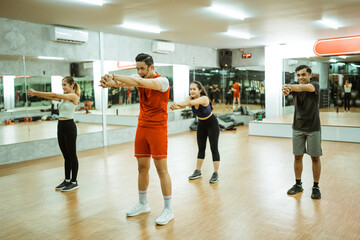 Group of asian men and women in sportswear doing arm muscle stretching with instructor in fitness center