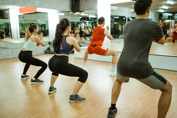 rear view of sporty group with instructor doing stance in fitness center