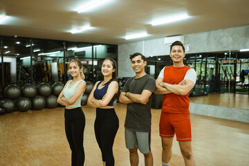 Sporty group of friends in sportswear standing with arms crossed after working out in fitness gym