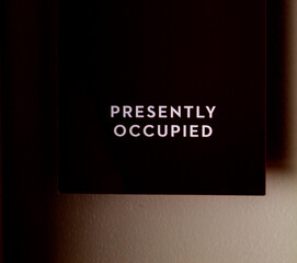 Black sign hanging on door that says Presently Occupied